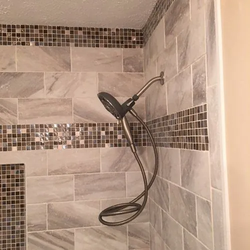 Tiled shower with a handheld shower head and mosaic band