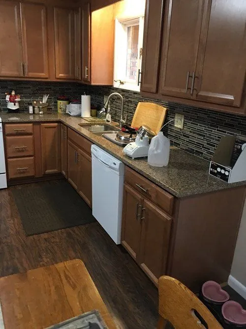L-shaped kitchen with dark countertop, glass tile backsplash and wood-look floor