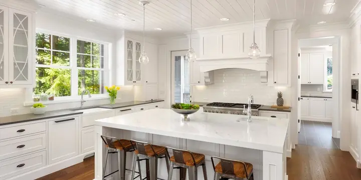 White remodeled kitchen with a large island, bar stools and hardwood floors